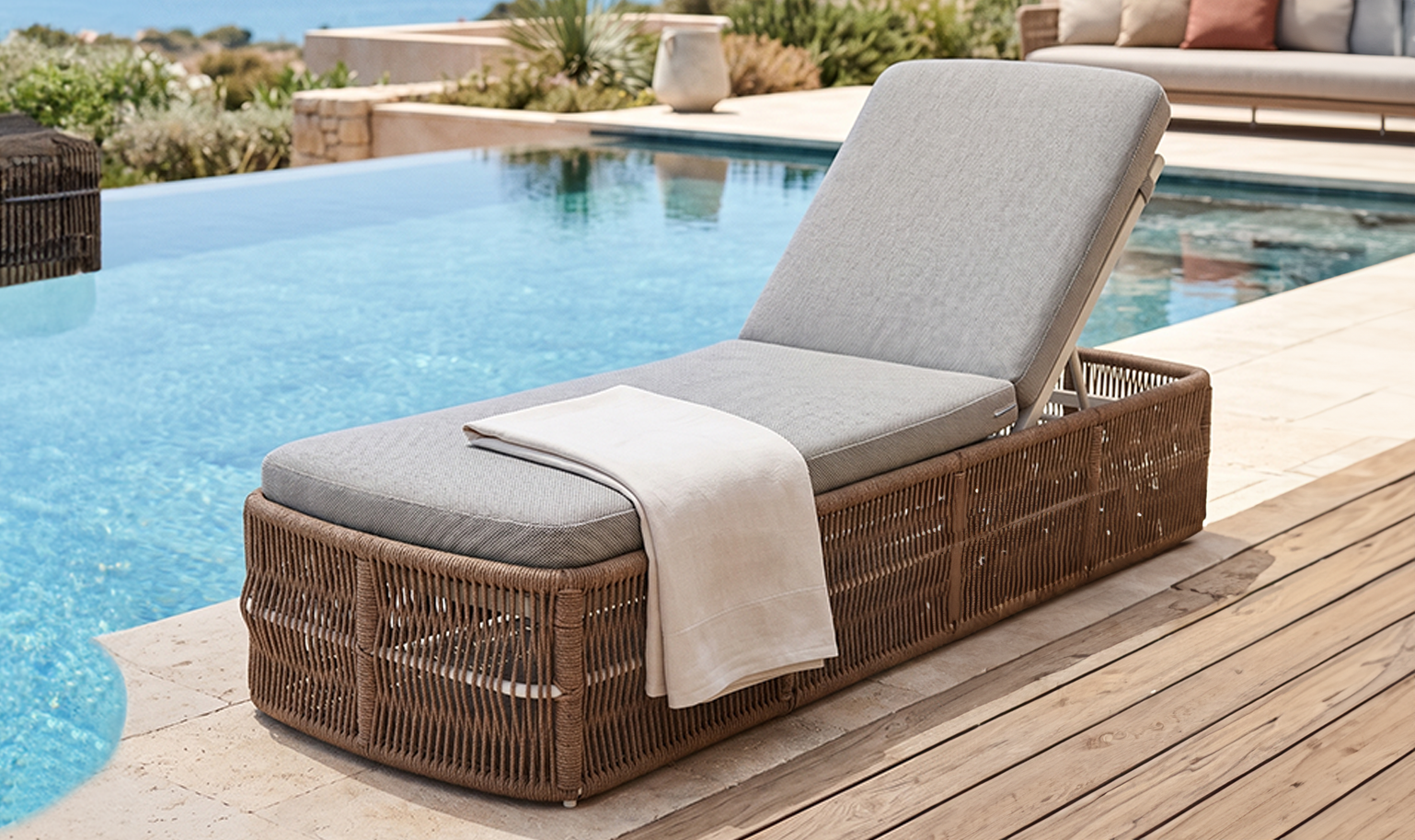 Elegant wicker chaise lounge with neutral cushion styled by a swimming pool in a serene outdoor setting
